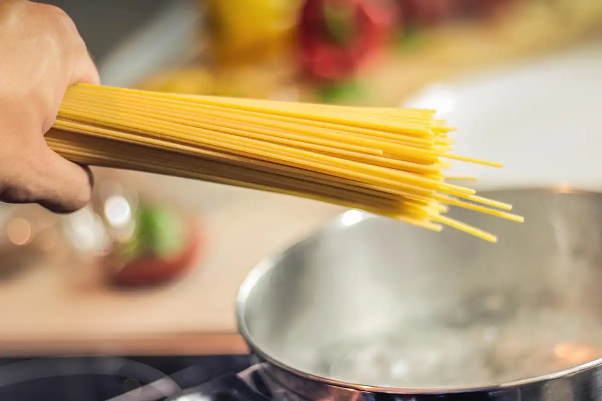 Mână care ține spaghete crude deasupra unei oale cu apă clocotită