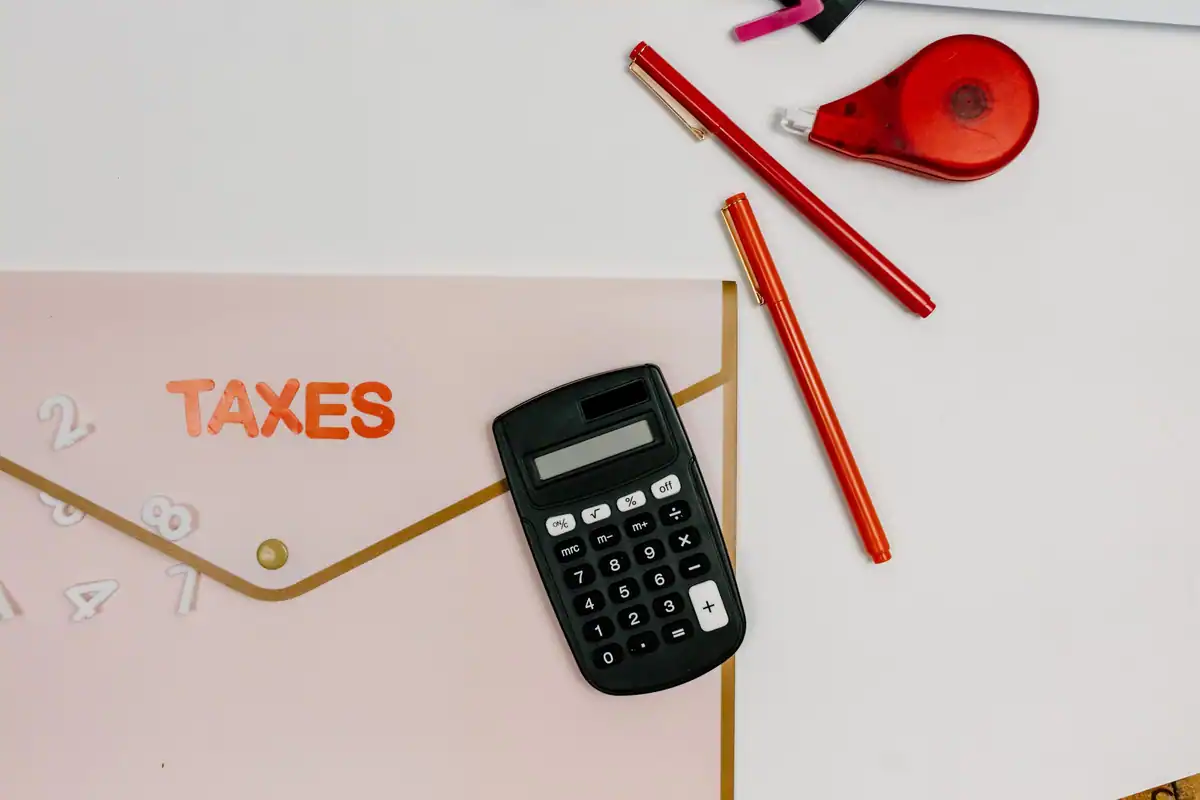 Calculator negru, pixuri roșii și un dosar cu hârtii pe o masă albă