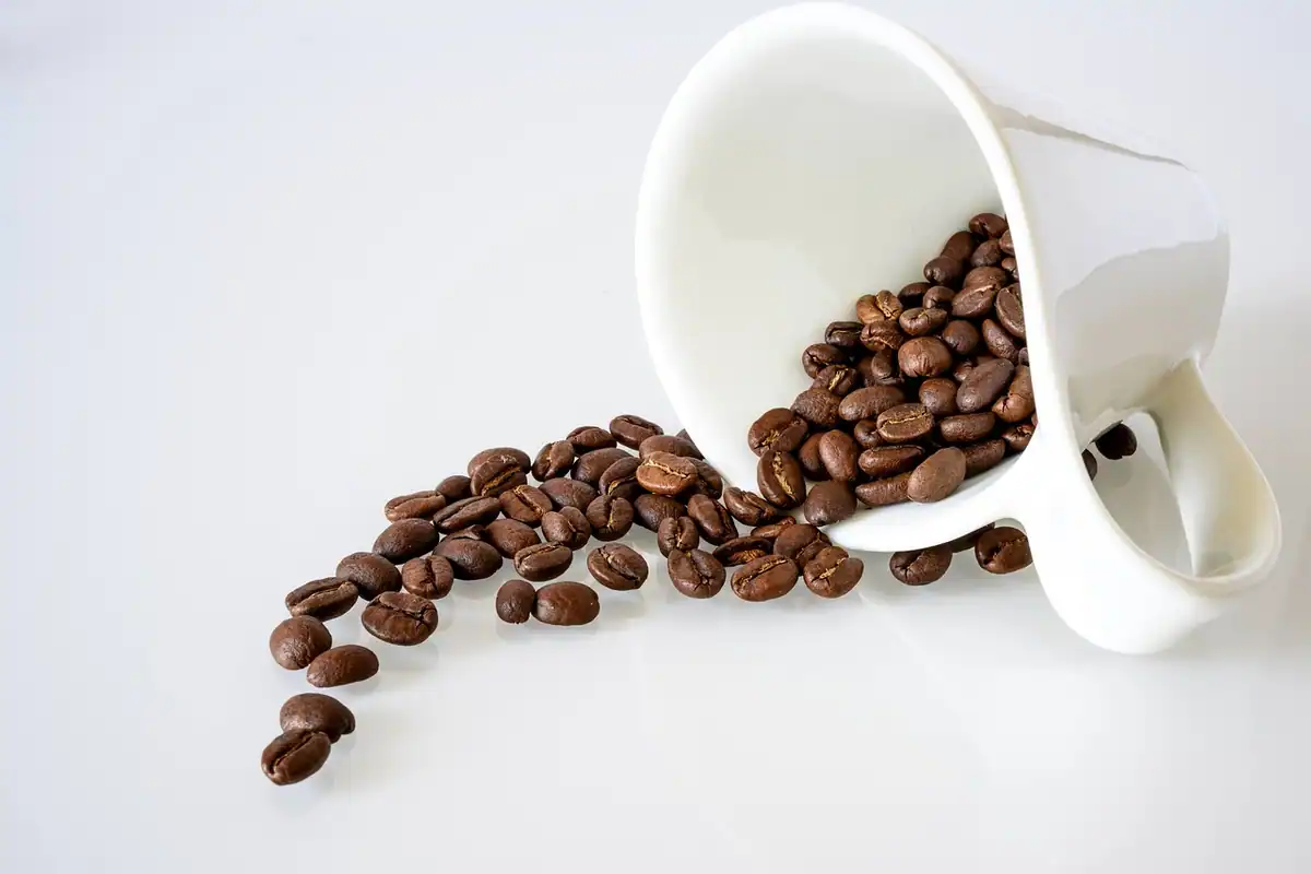 Monede răspândite pe o masă lângă o ceașcă de cafea, exemplu de cheltuieli mici care se adună