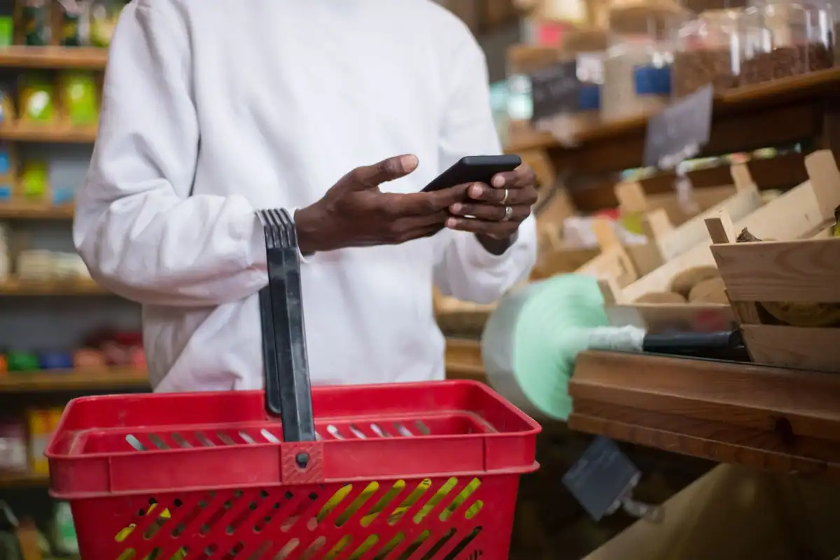 Bărbat care face cumpărături cu telefonul în mână și un coș roșu cu alimente