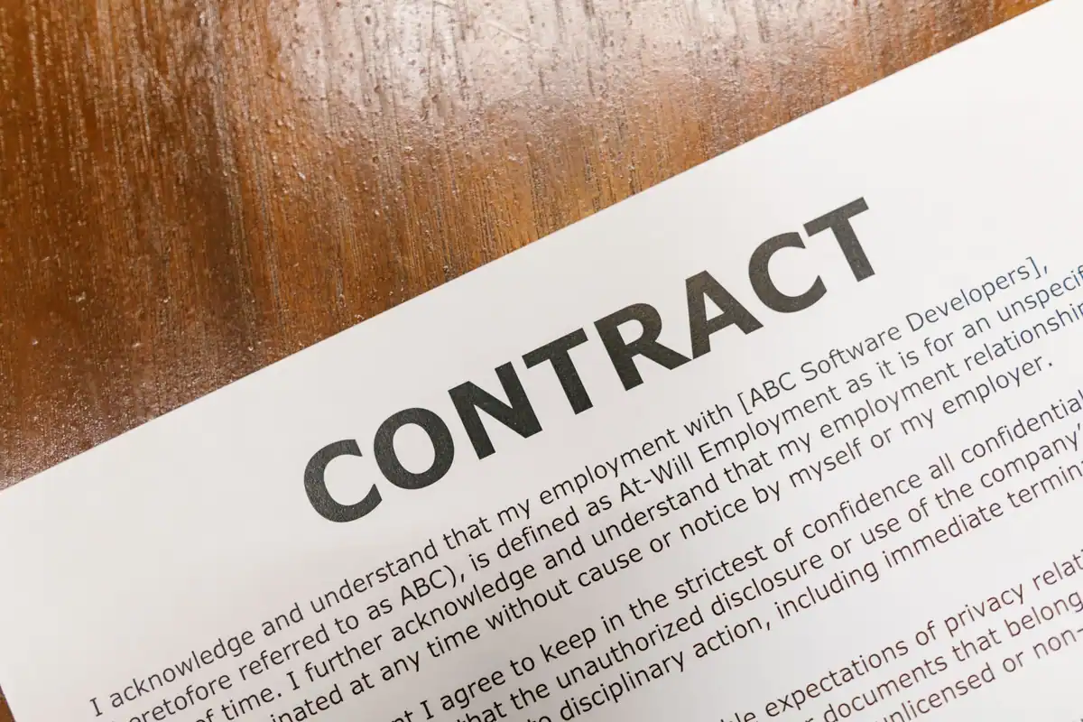 Contract tipărit, cu rânduri mici de text, așezat pe o masă de lemn