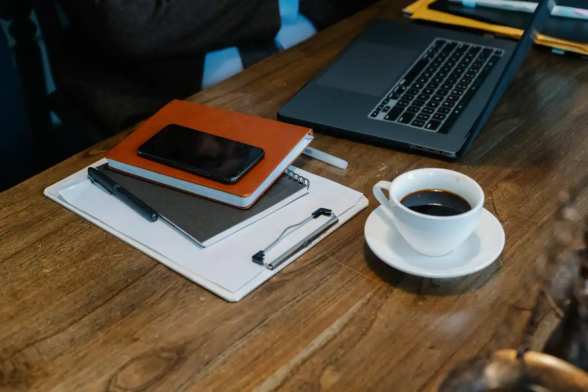 Telefon, agendă, laptop și o cană de cafea pe o masă de lemn