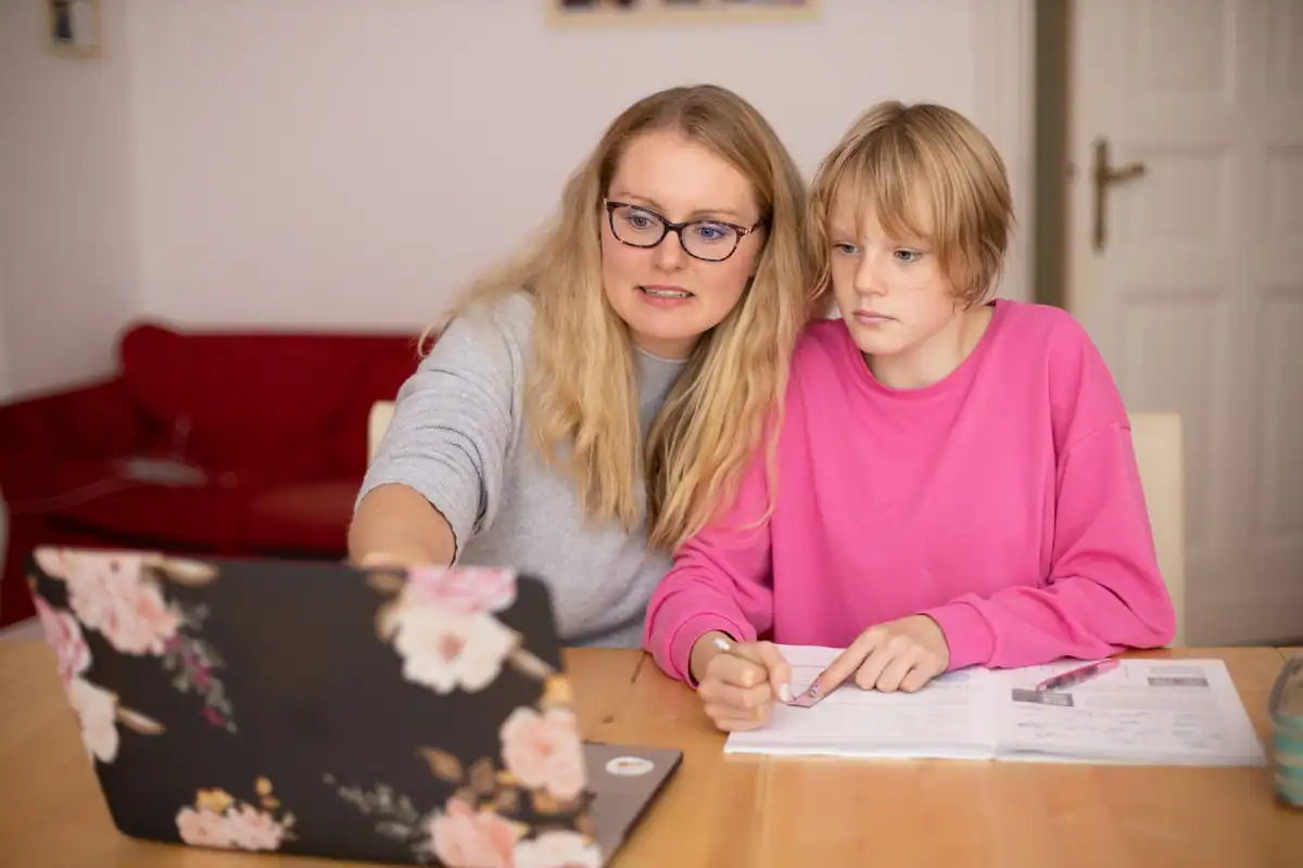 Mamă și copil care fac temele împreună la o masă, cu laptopul alături