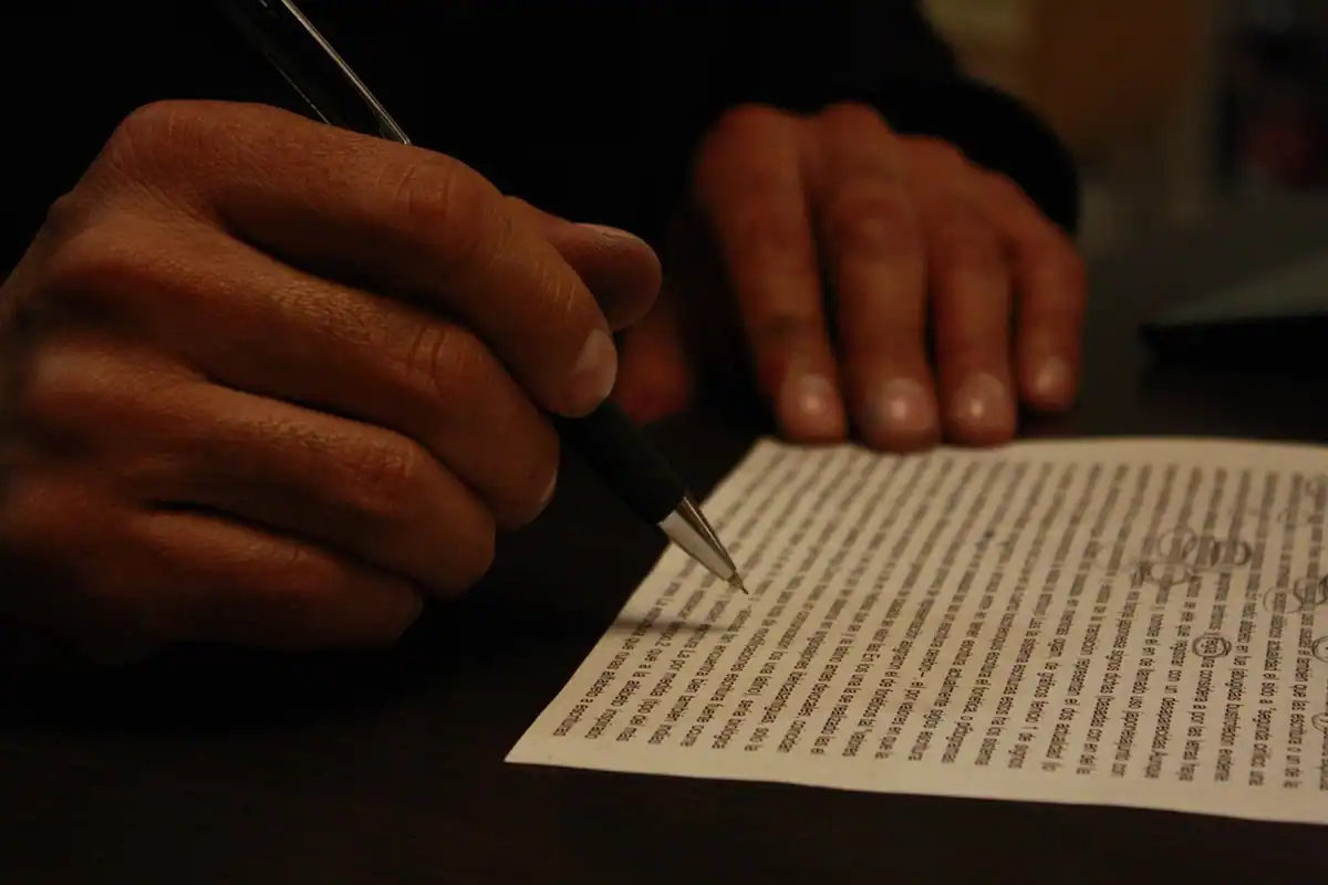 Mână care semnează cu un pix un contract pe birou, imagine a angajamentului de garant