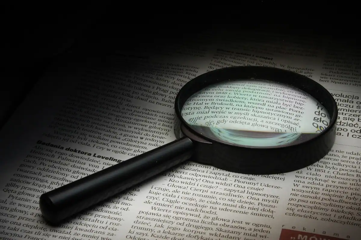 Lupă neagră așezată deasupra unui text tipărit de ziar