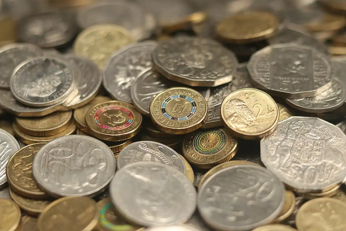 Două grămezi de monede pe o masă de lemn, pentru împărțirea banilor între nevoi și dorințe
