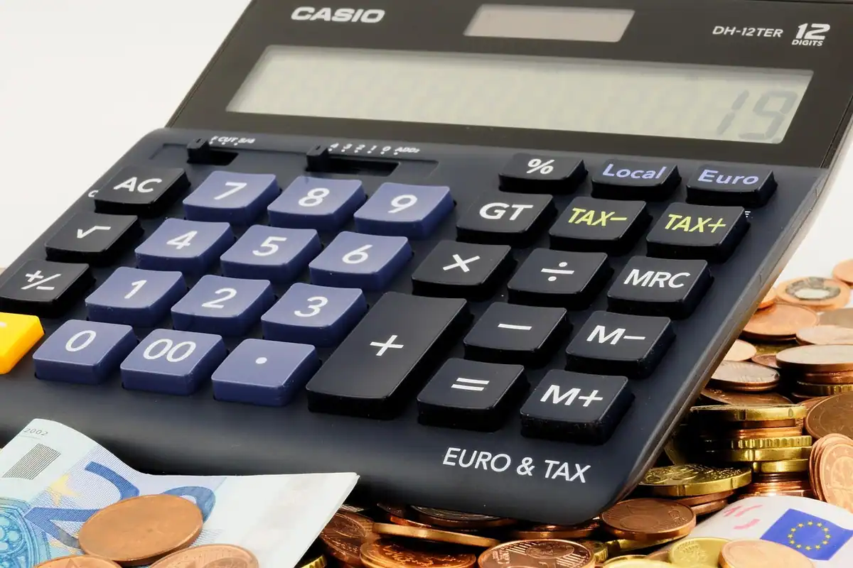 Pușculiță lângă un calculator și hârtii, pentru calculul rambursării anticipate a creditului