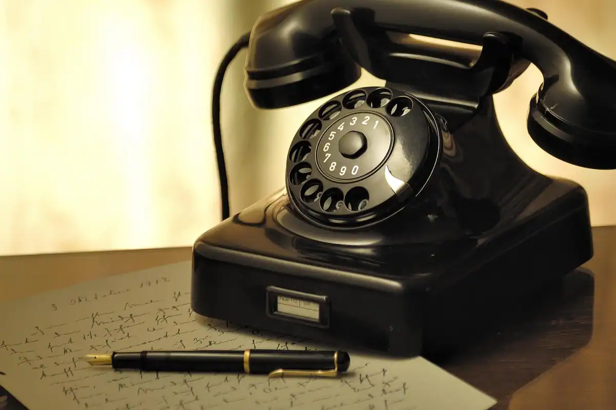 Telefon negru cu disc, vechi, lângă un pix cu peniță pe hârtii