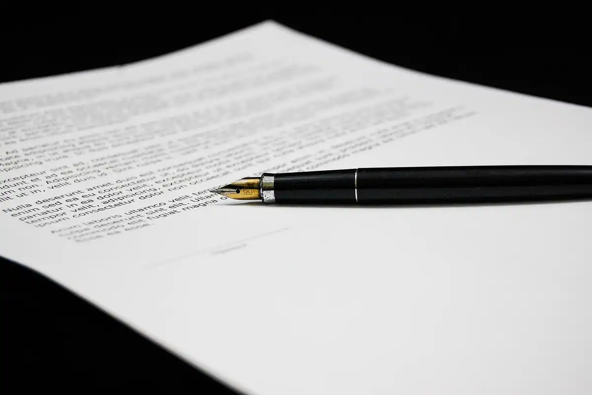 Contract tipărit pe o masă neagră, cu un stilou așezat peste text